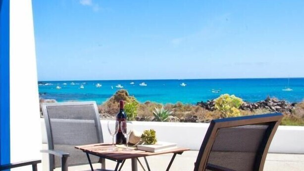 Un balcon avec une table, une chaise et une vue sur l’océan, où l’on peut apercevoir des bateaux.
