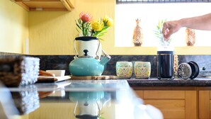 A kitchen counter with a blue kettle, a vase with flowers, and a hand pouring something into a black container.