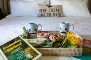 Un plateau de petit-déjeuner soigneusement préparé est posé sur un lit, avec deux tasses, un livre et un coussin orné de motifs.