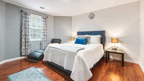 Une chambre à coucher avec un lit, des tables de chevet, une chaise, une fenêtre avec des rideaux et une horloge murale.
