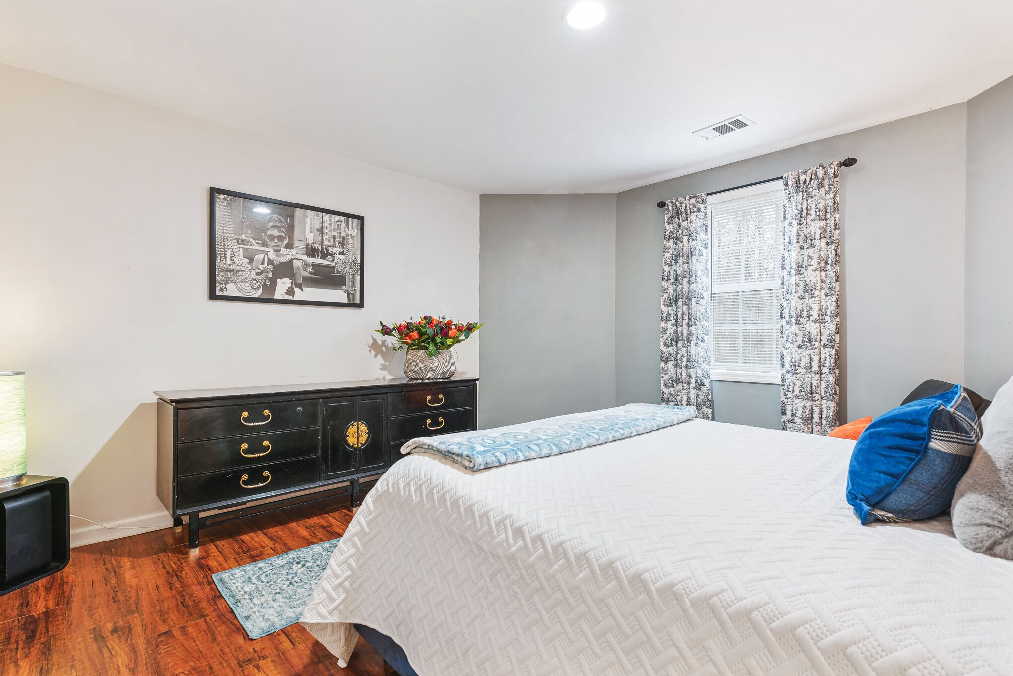 A bedroom with a bed, a dresser, a picture on the wall, and a window with curtains.