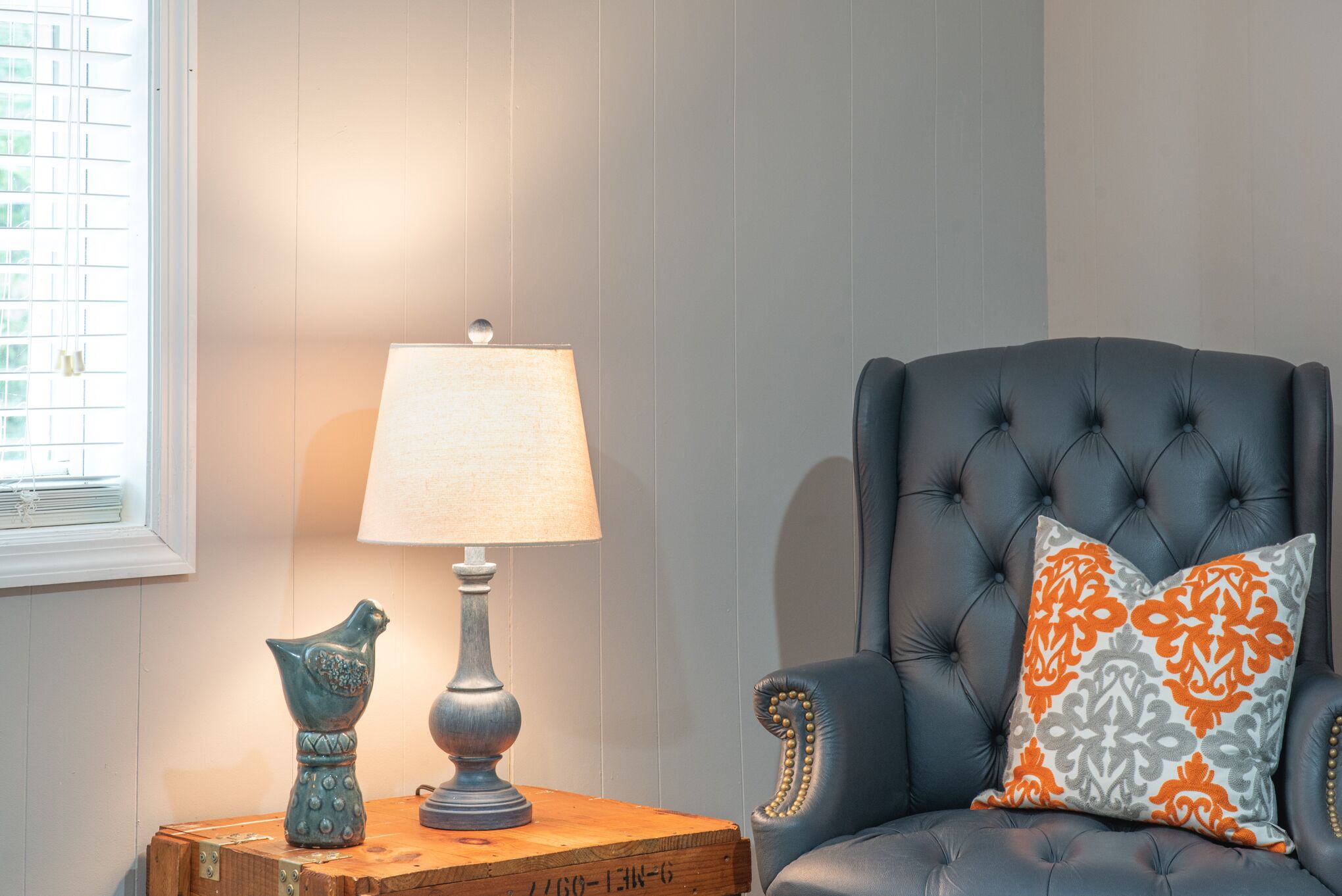 A room with a tufted armchair, a lamp, and decorative items on a wooden side table.