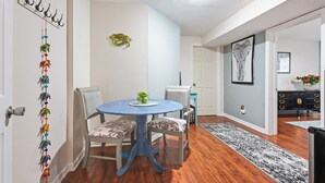 Un coin repas avec une table bleue et deux chaises, un porte-manteau avec des crochets, une chaise à motifs zébrés, un tapis noir et blanc, et une porte donnant sur une autre pièce.