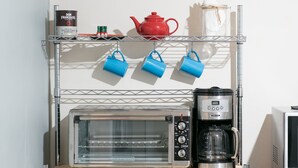 Une cuisine équipée d’un four grille-pain, d’une machine à café et d’une étagère sur laquelle se trouvent une théière rouge, des tasses bleues et une boîte de café.