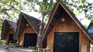 A row of thatched-roof cottages with large sliding doors, wooden benches, and a concrete pathway leading to the entrance. - Set amidst lush greenery and azure waters of the Pacific Ocean. (Surigao)