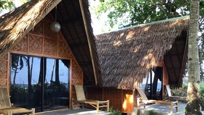 A thatched-roof hut with a large sliding glass door, wooden furniture, and a small fire pit. - Set amidst lush greenery and azure waters of the Pacific Ocean. (Surigao)