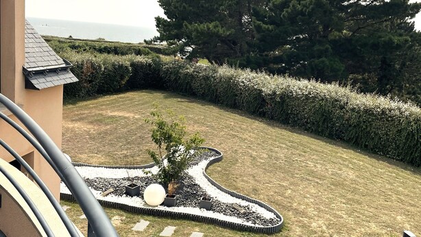 A landscaped garden with a winding path, a large tree, and a view of the sea.