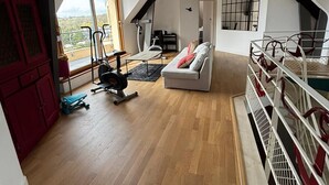 A loft-style room with a wooden floor, a white sofa, a red cabinet, and a window with a view.