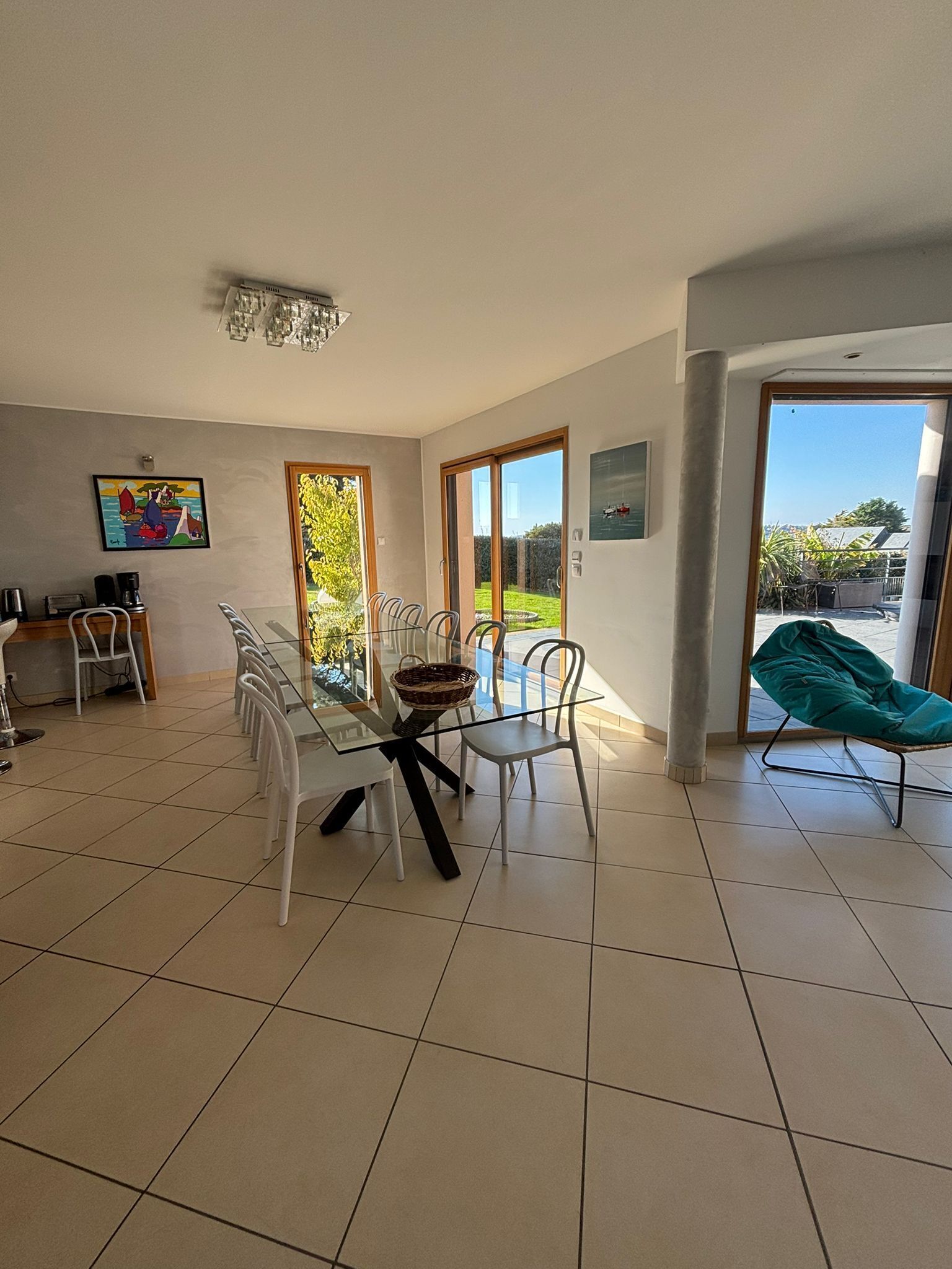 Un comedor con mesa de vidrio, sillas y vista a un jardín a través de puertas de cristal.