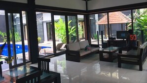 A spacious indoor area with a large glass wall, a sofa, a coffee table, and a television. - Villa Glas (Kerobokan)