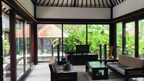 A spacious living area with a large glass wall, a flat-screen TV, and a comfortable seating arrangement. - Villa Glas (Kerobokan)