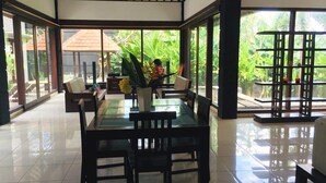 A spacious indoor area with a glass dining table surrounded by chairs, a sofa, and a small table with a vase of flowers. - Villa Glas (Kerobokan)