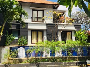 A two-story building with a balcony, surrounded by lush greenery and a blue-tiled wall. - Villa Glas (Kerobokan)