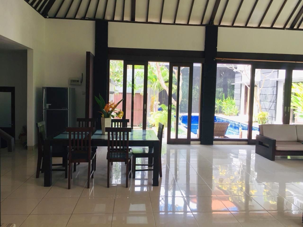A spacious room with a tiled floor, a dining table with chairs, a refrigerator, and a large sliding glass door leading to a pool area.