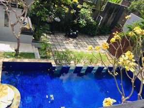 A swimming pool with blue tiles, surrounded by greenery and a paved area with a scooter. - Villa Glas (Kerobokan)