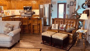Un salon chaleureux avec un canapé en cuir marron, un fauteuil gris et un tapis à motifs.