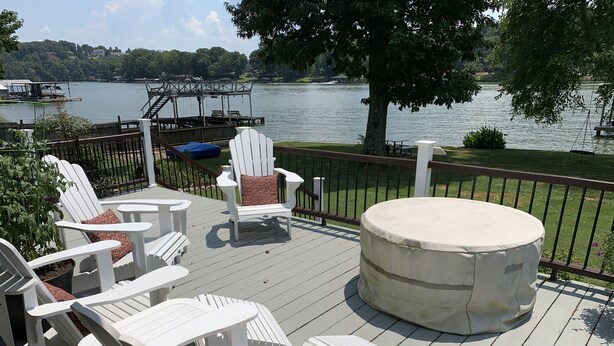Une terrasse dotée de chaises Adirondack blanches, d’une table ronde et d’un espace salon couvert offrant une vue sur un lac.