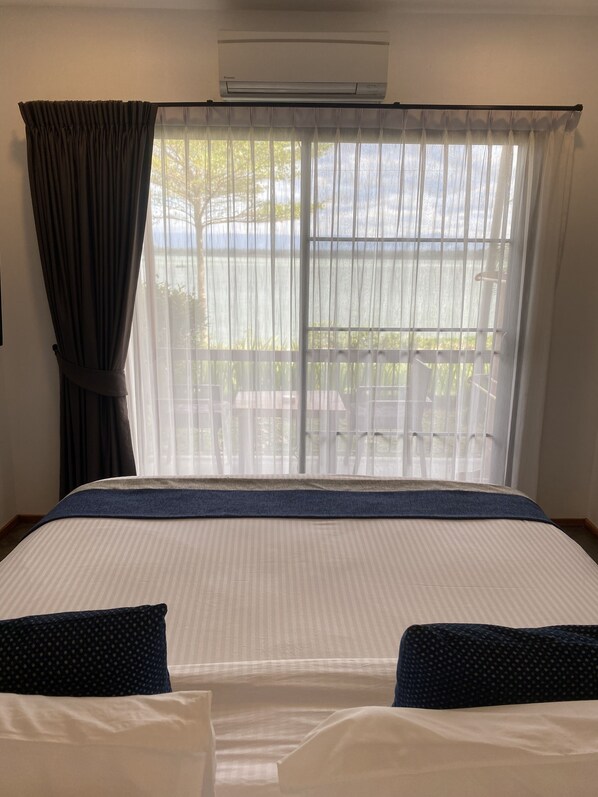 Une chambre d’hôtel avec un grand lit, une fenêtre avec des rideaux légers et un appareil de climatisation placé au-dessus de la fenêtre.