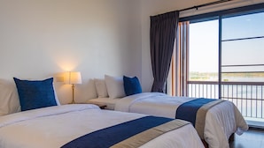 A hotel room with two beds, a nightstand, a lamp, and a large window with a view of the outdoors.