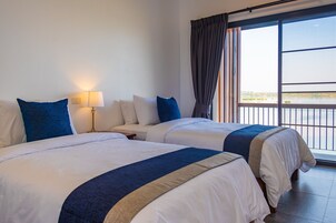 Habitación de hotel con dos camas, una mesita de noche, una lámpara y un ventanal con vistas al exterior.