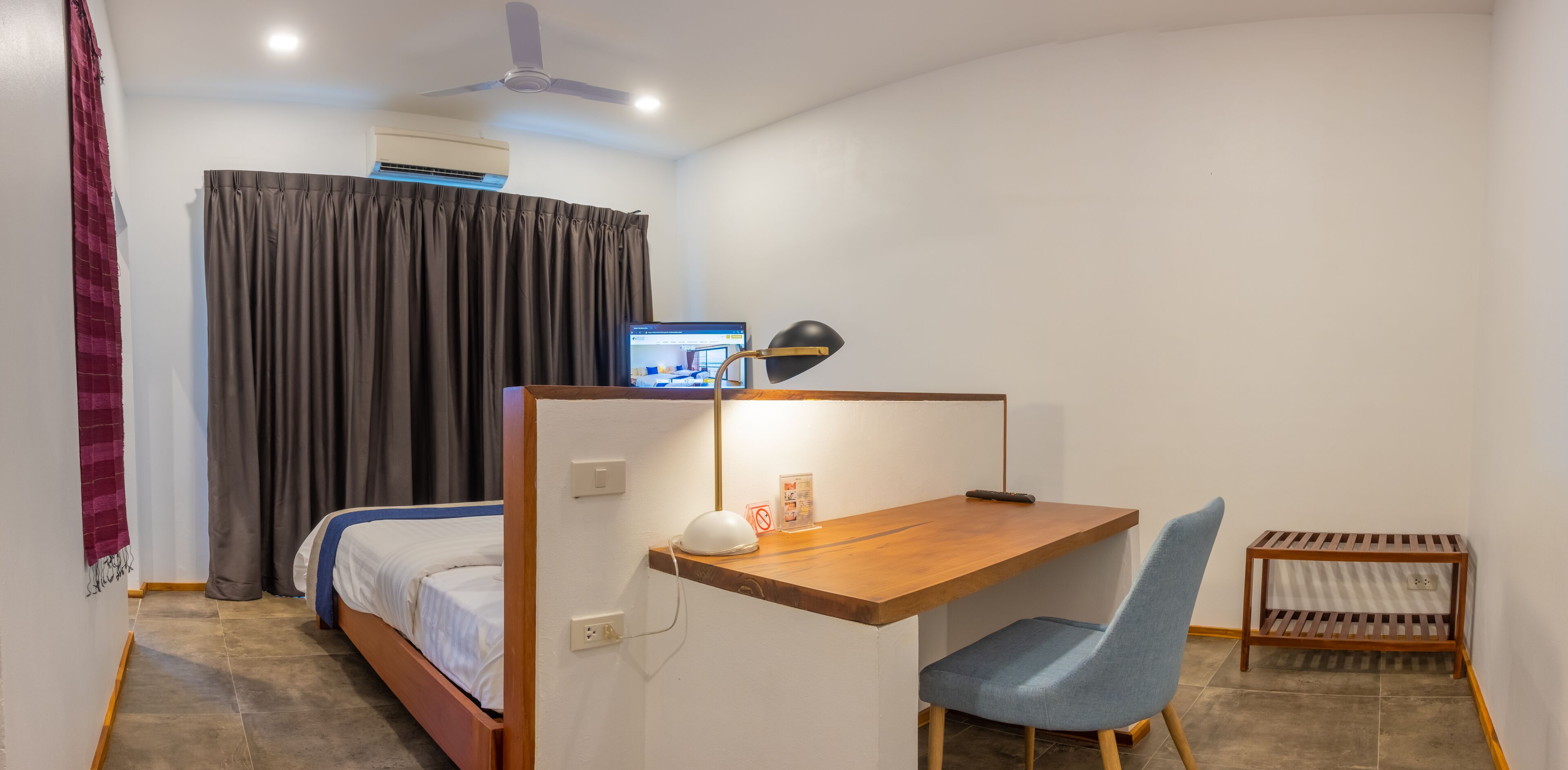 A bedroom with a bed, a desk with a chair, a ceiling fan, and a window with curtains.