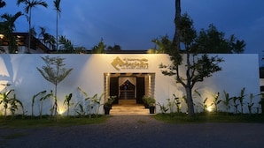 A hotel entrance with a sign, a staircase, and surrounding greenery.