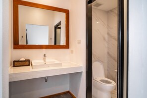 A bathroom with a white sink, a wooden-framed mirror, and a toilet with a marble wall. - The Riviera Champasak (Champasak)