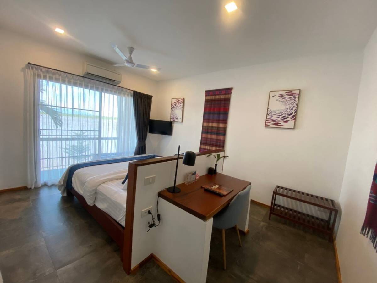 A bedroom with a bed, a desk, a chair, a radiator, and a window with curtains.