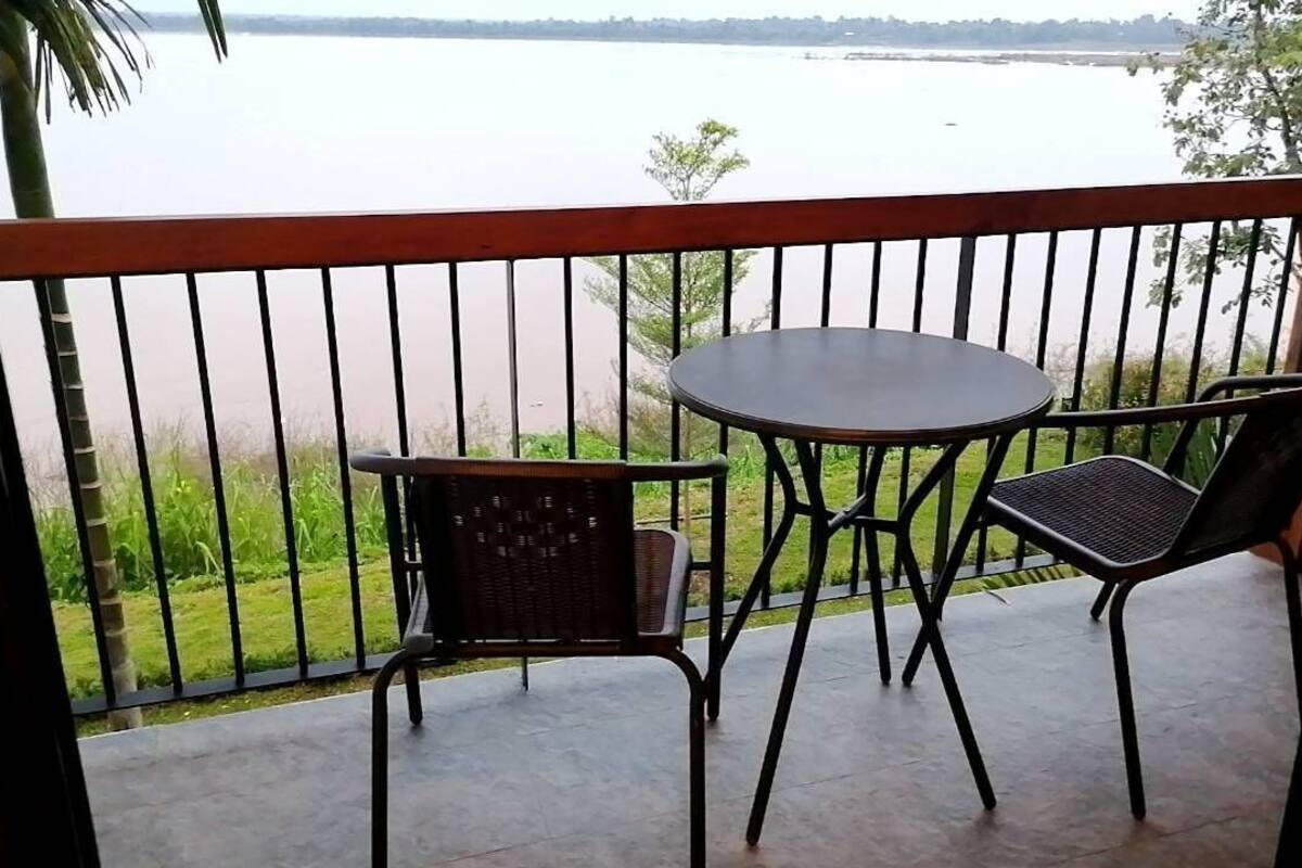Un balcón con una mesa y dos sillas, con vista a una masa de agua tranquila.