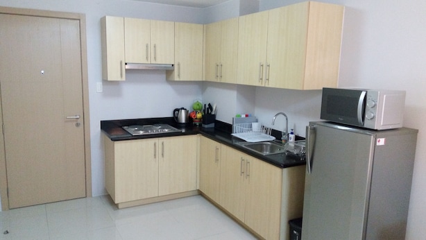 A compact kitchen with light wooden cabinets, a black countertop, a stove, a sink, a microwave, and a refrigerator. - Grass homes 2 bedrooms (Bago Bantay)