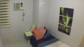 A small, compact room with a bed, a chair, and a wall-mounted air conditioning unit. - Grass homes 2 bedrooms (Bago Bantay)