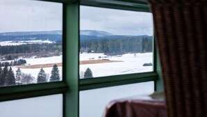 Una habitación con un ventanal que ofrece vistas a un paisaje nevado con árboles y montañas distantes.