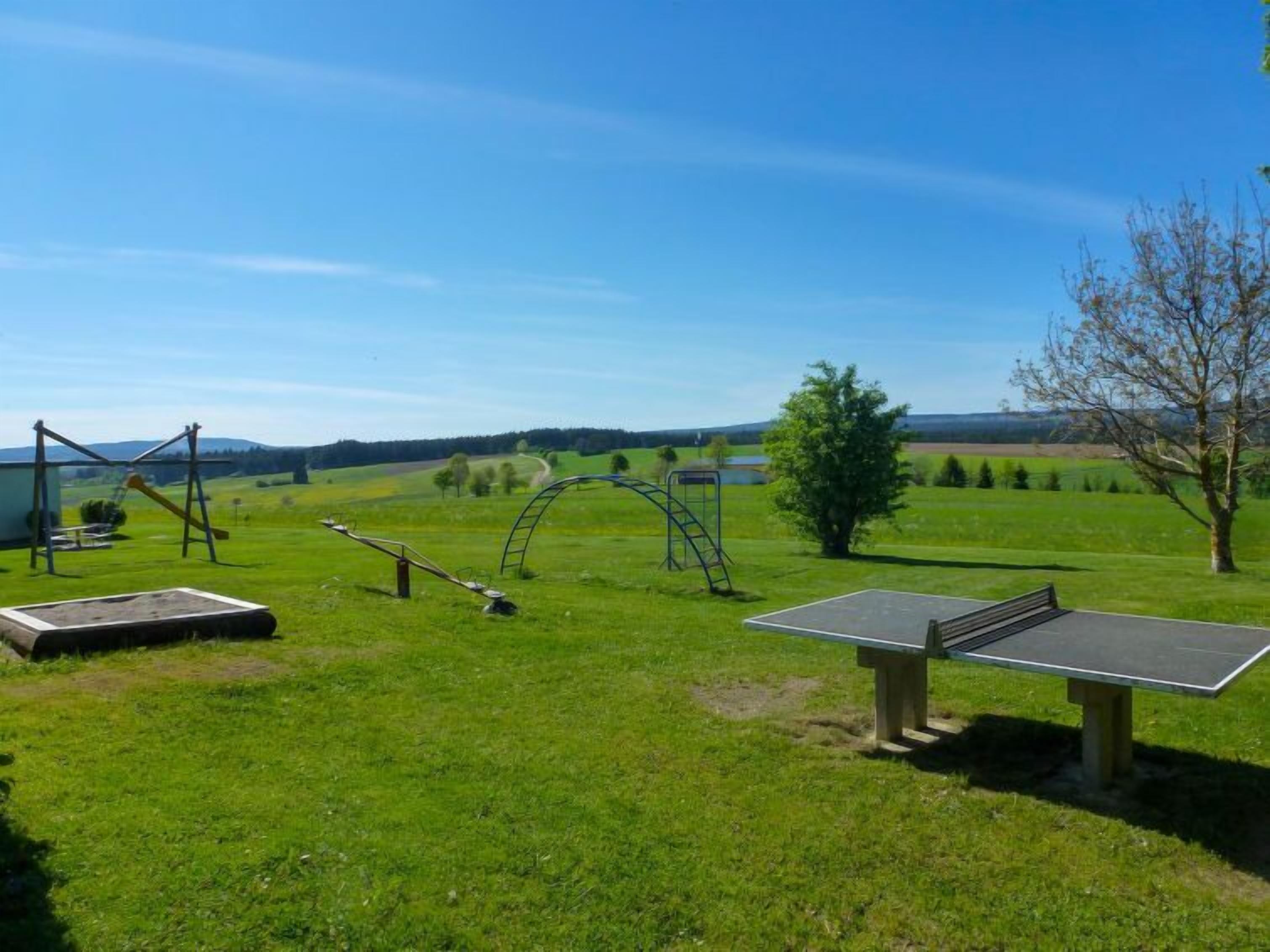 A playground with swings and a climbing structure in a grassy field with a clear sky.