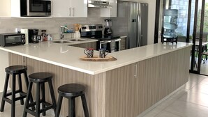 A modern kitchen with white cabinetry, a large island with stools, a refrigerator, and a water dispenser. - Exclusive Gated Community with HD TV, Air Conditioning, Cable and Netflix  (Nuevo Cuscatlán)