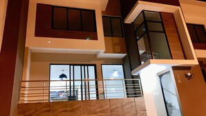 A modern multi-story building with large windows, a balcony, and a visible staircase. - Exclusive Gated Community with HD TV, Air Conditioning, Cable and Netflix  (Nuevo Cuscatlán)