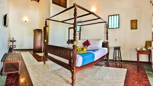 A four-poster bed with a marble floor, a wooden cabinet, and a small stool.