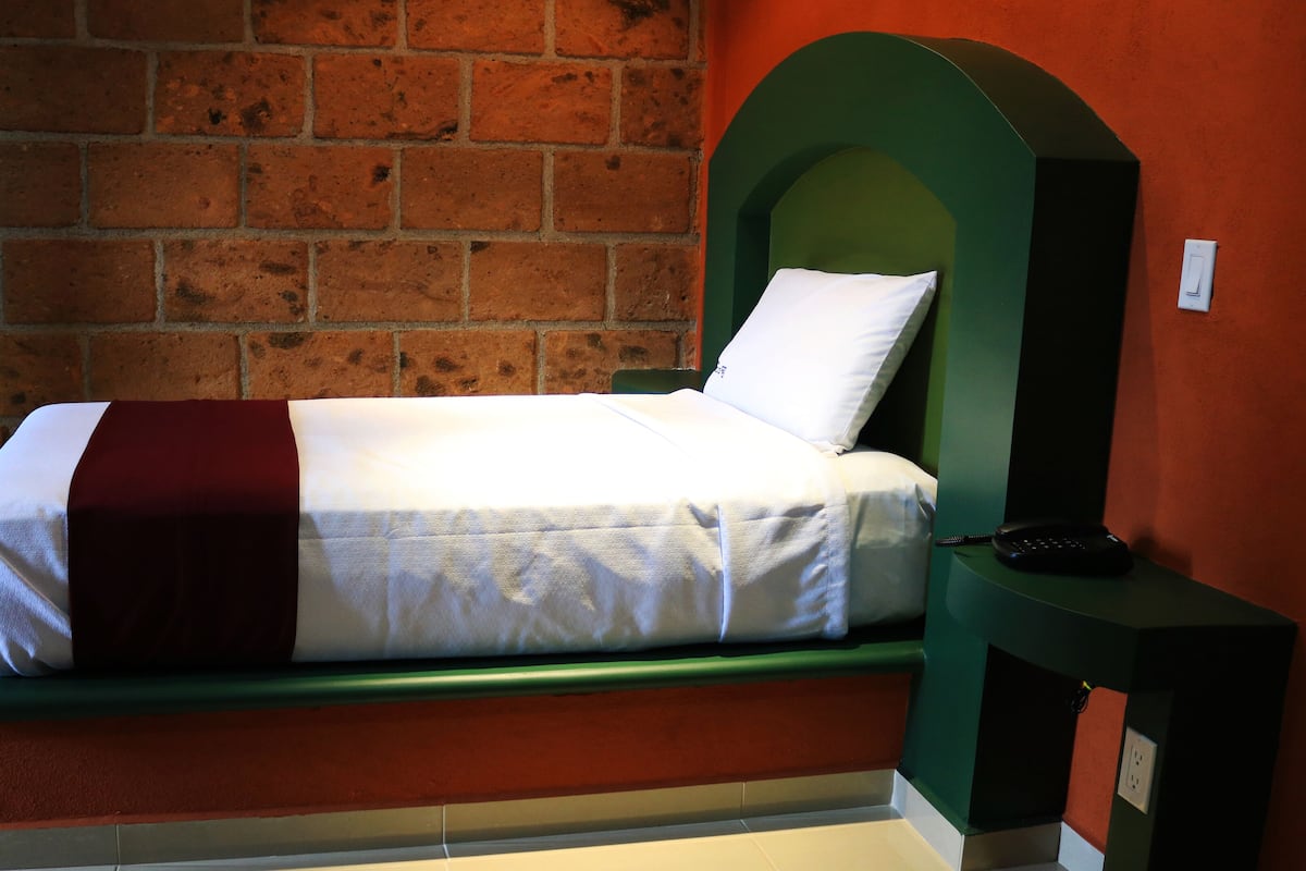 Een bed met een witrood beddegoed, een groen hoofdeinde en een nachtkastje met een afstandsbediening.