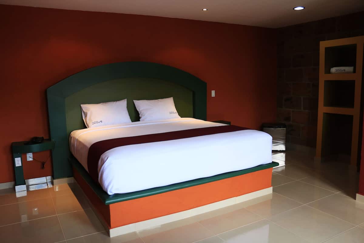Een keurig opgemaakt bed met witte beddengoed en een groen hoofdeinde in een kamer met rode wanden en een betegelde vloer.