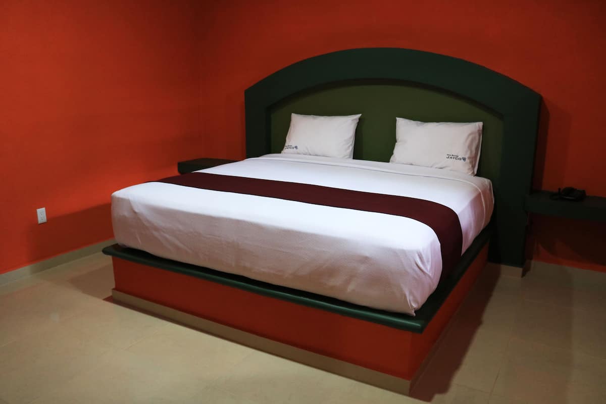 Een bed met een groen hoofdeinde, witte beddengoed en een rode accentkleur.