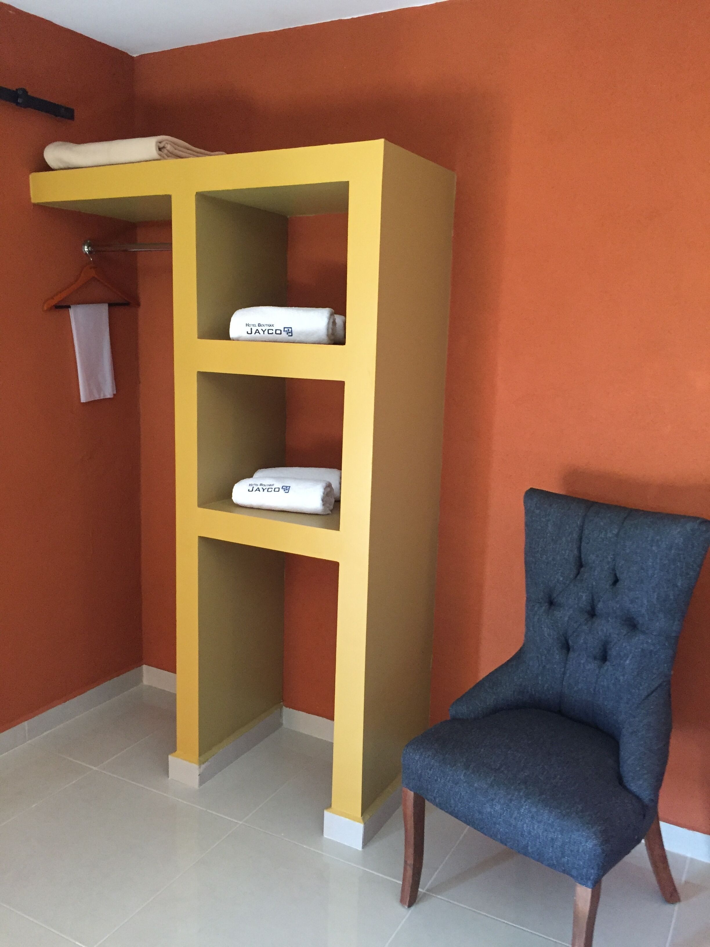A room with a yellow shelving unit, a blue upholstered chair, and a white towel hanging on a rack.