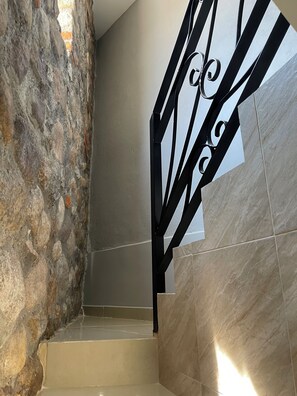 A staircase with a stone wall on one side and a tiled wall on the other, leading to an upper floor. - Hotel Boutique Jayco (San José Iturbide)