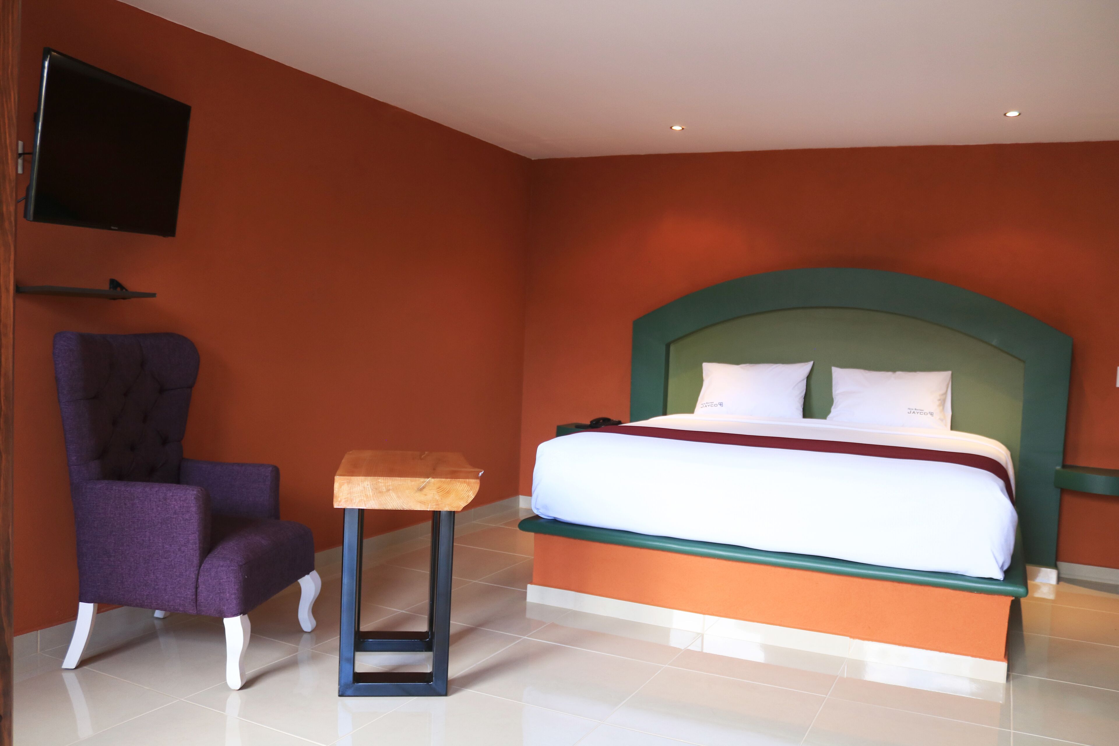 Una habitación de hotel con una cama, una silla, una mesita y un televisor montado en la pared.
