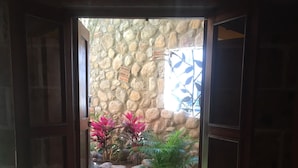 A window with a view of a stone wall and a garden with rocks, plants, and a water feature. - Hotel Boutique Jayco (San José Iturbide)