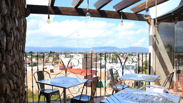 A terrace with metal tables and chairs, a stone wall, and a view of distant buildings and mountains. - Hotel Boutique Jayco (San José Iturbide)
