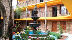 A courtyard with a central fountain, surrounded by a variety of flowers and plants, and a brick building with balconies. - Hotel Boutique Jayco (San José Iturbide)
