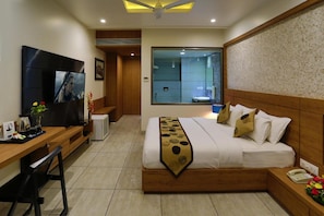 A hotel room with a bed, a desk, a TV, a bathroom, and a view through a large window.