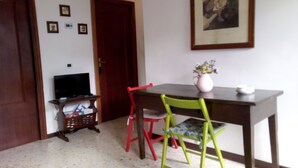 A room with a wooden door, a television on a stand, a table with a vase and a cup, and colorful chairs.