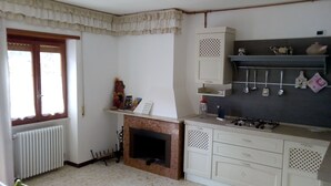 A kitchen with a gas stove, white cabinets, a window with curtains, and a radiator.