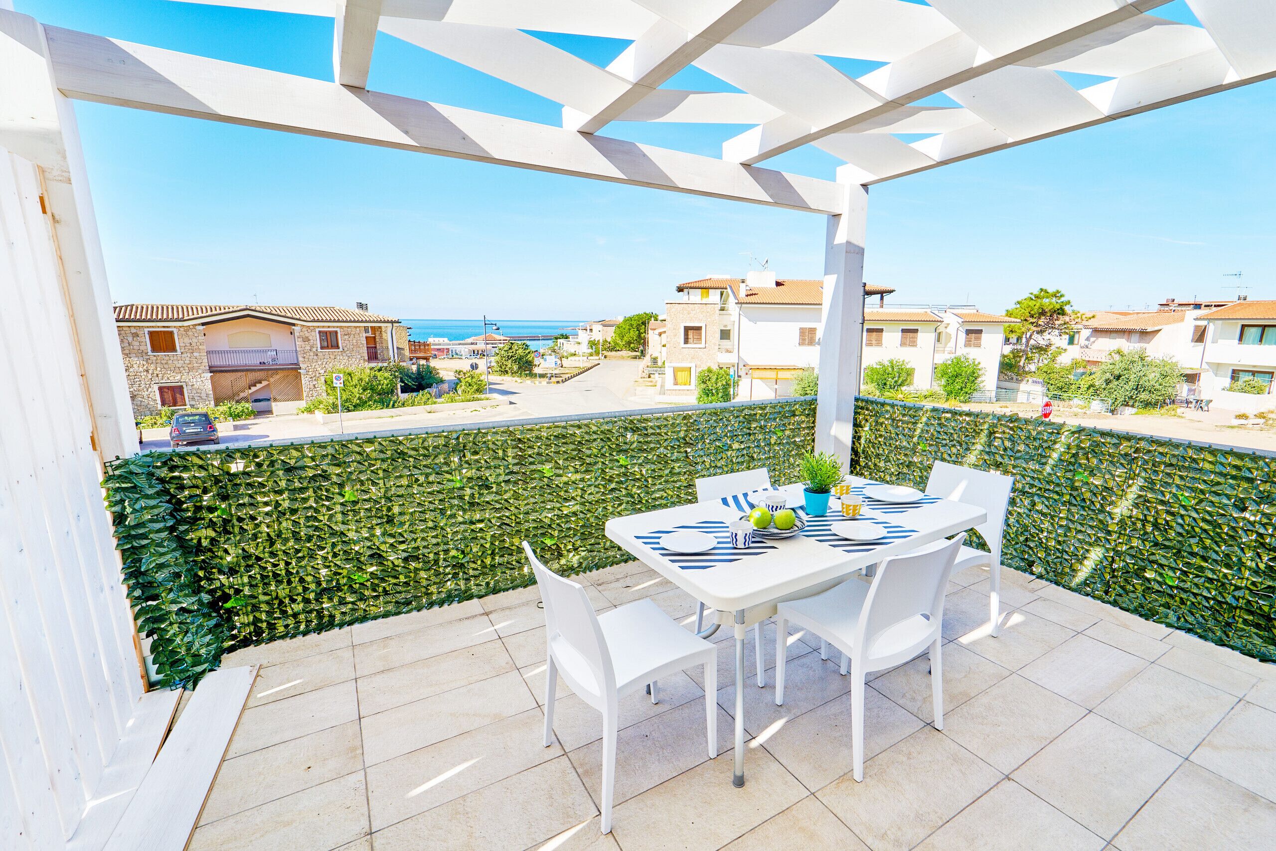 Ein Balkon mit Tisch und Stühlen, Blick auf das Meer und eine weiße Pergola.