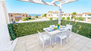 Un balcon avec une table et des chaises, une vue sur la mer et une pergola blanche.